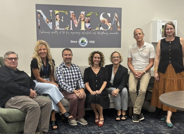 NEMCSA staff joined by MSHDA and MCA staff sitting together in front of NEMCSA sign